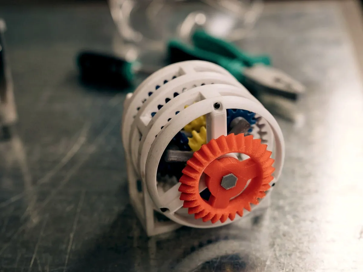 Prototip funcional imprès en 3D: un mecanisme d’engranatges de colors sobre un banc de treball metàl·lic