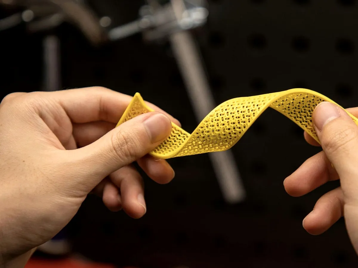 Dues mans doblegant una tira de TPU groc imprès en 3D, amb estructura de malla, que es torça sense trencar-se